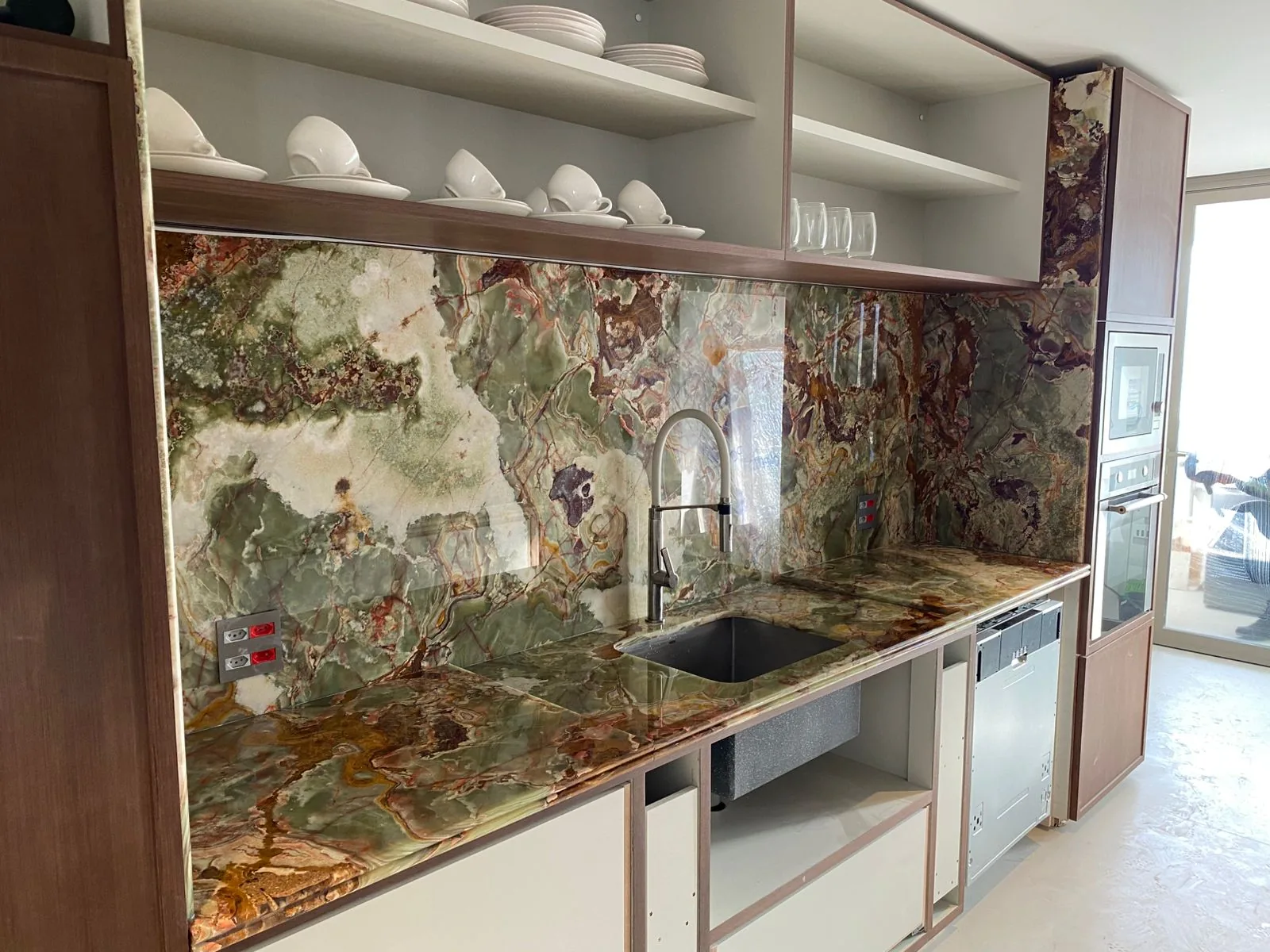 Painel de parede em ônix verde com veios casados integrado à bancada de cozinha